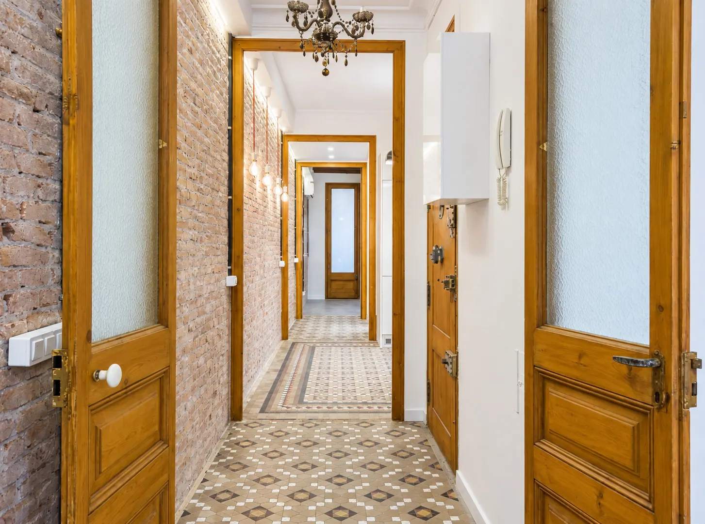 AvN long hallway with brick wall, wooden door frames and hanging Edison bulbs over tiled floor