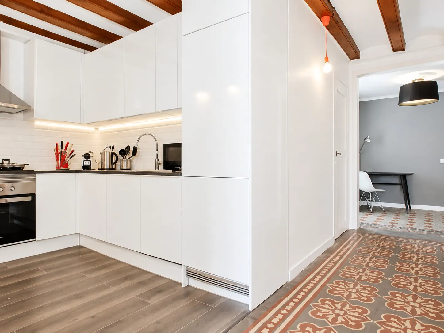 LLn white kitchen with exposed timber beams opening onto the tiled hallway