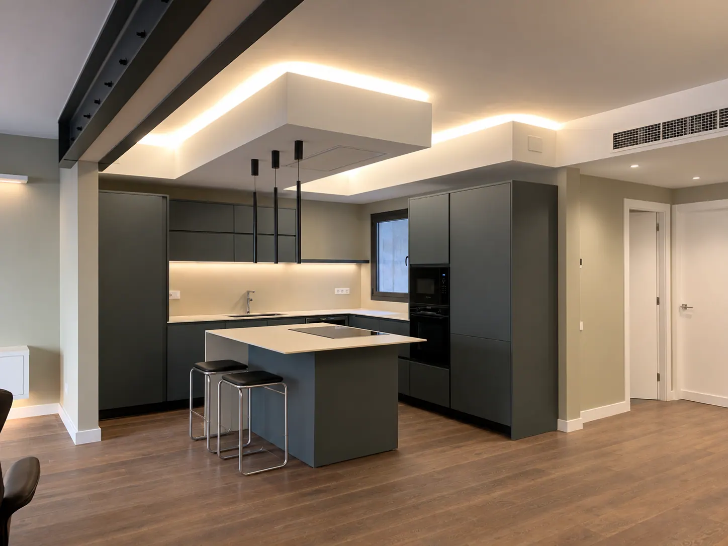 BiG kitchen island with cream countertop and dark green base, black pendant lights and warm wood flooring