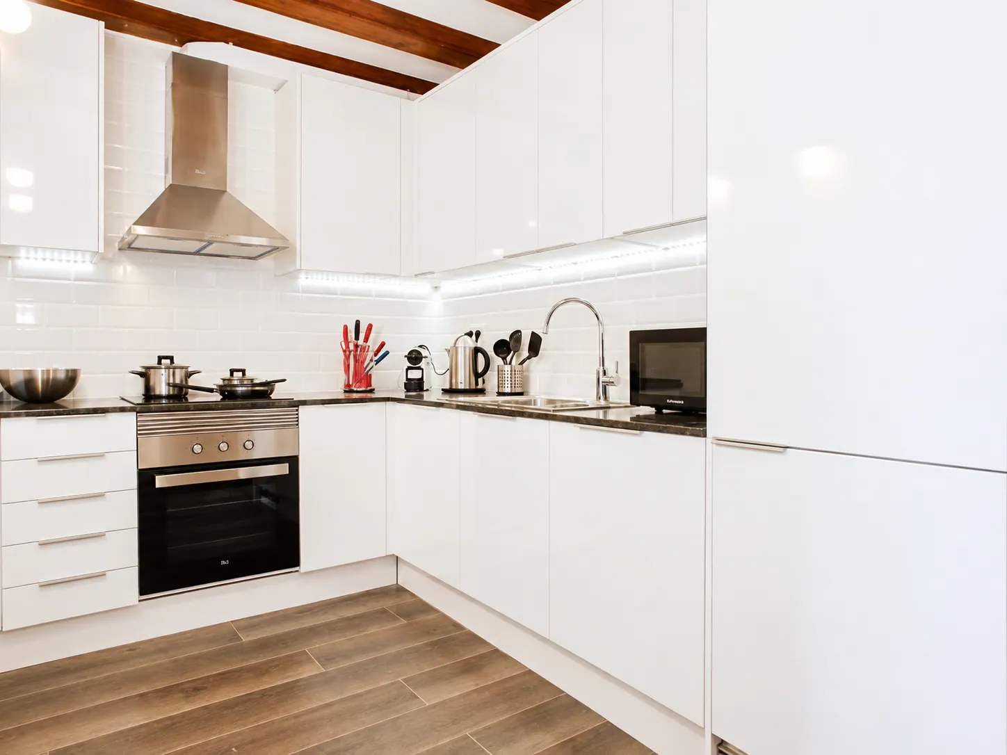LLn kitchen run with white cabinets, dark worktop, stainless extractor and timber beam ceiling