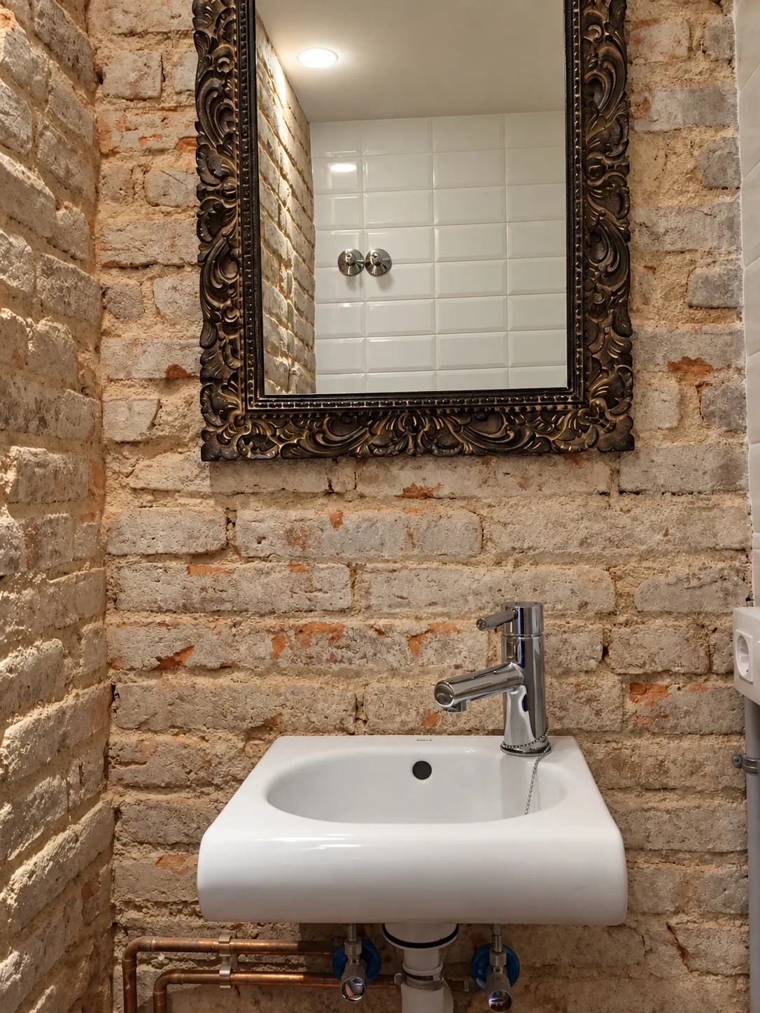 TrF bathroom basin with ornate framed mirror on an exposed brick wall and copper pipework