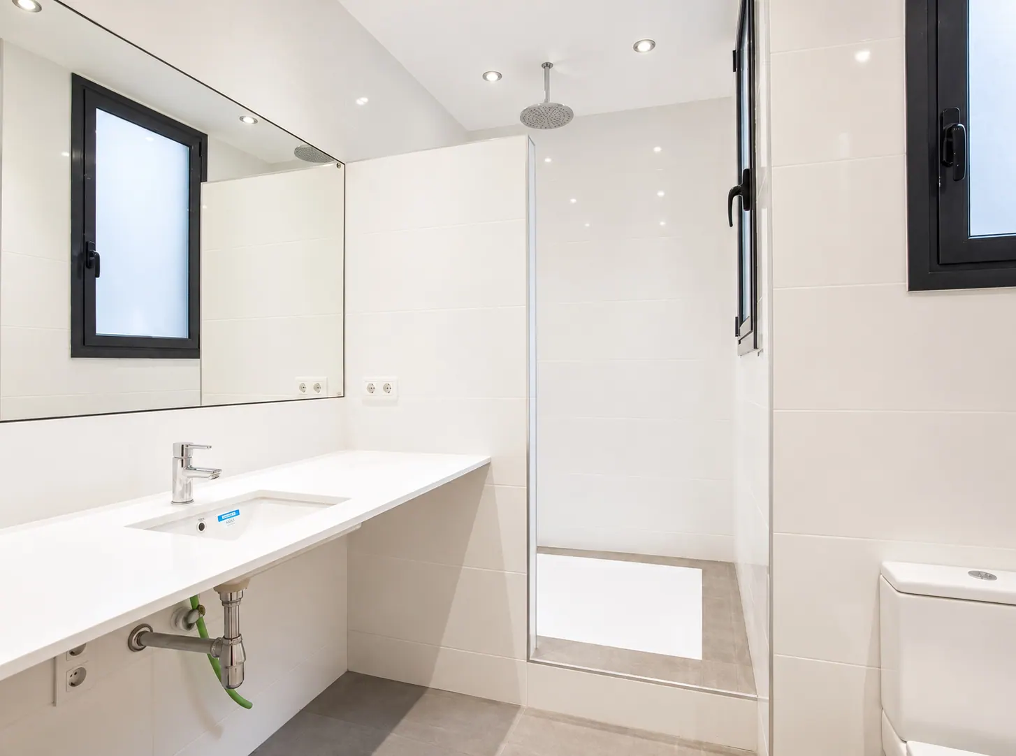 AvN minimalist bathroom with white ceramic tiles and chrome fixtures under recessed lighting