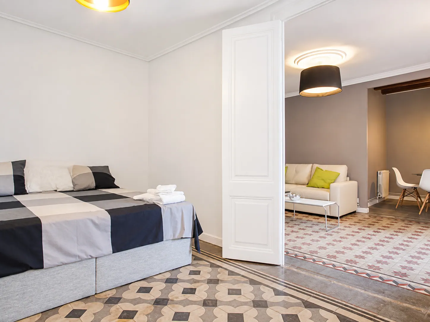 LLn bedroom with grey bedding and panelled door opening onto the living room