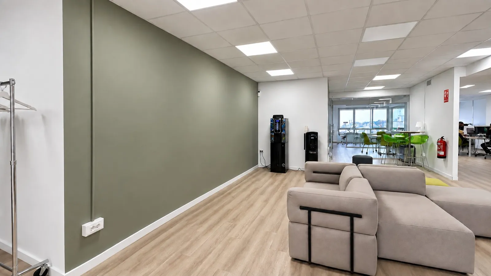 GlG breakout lounge with olive green feature wall and beige modular sofa beside the open workspace