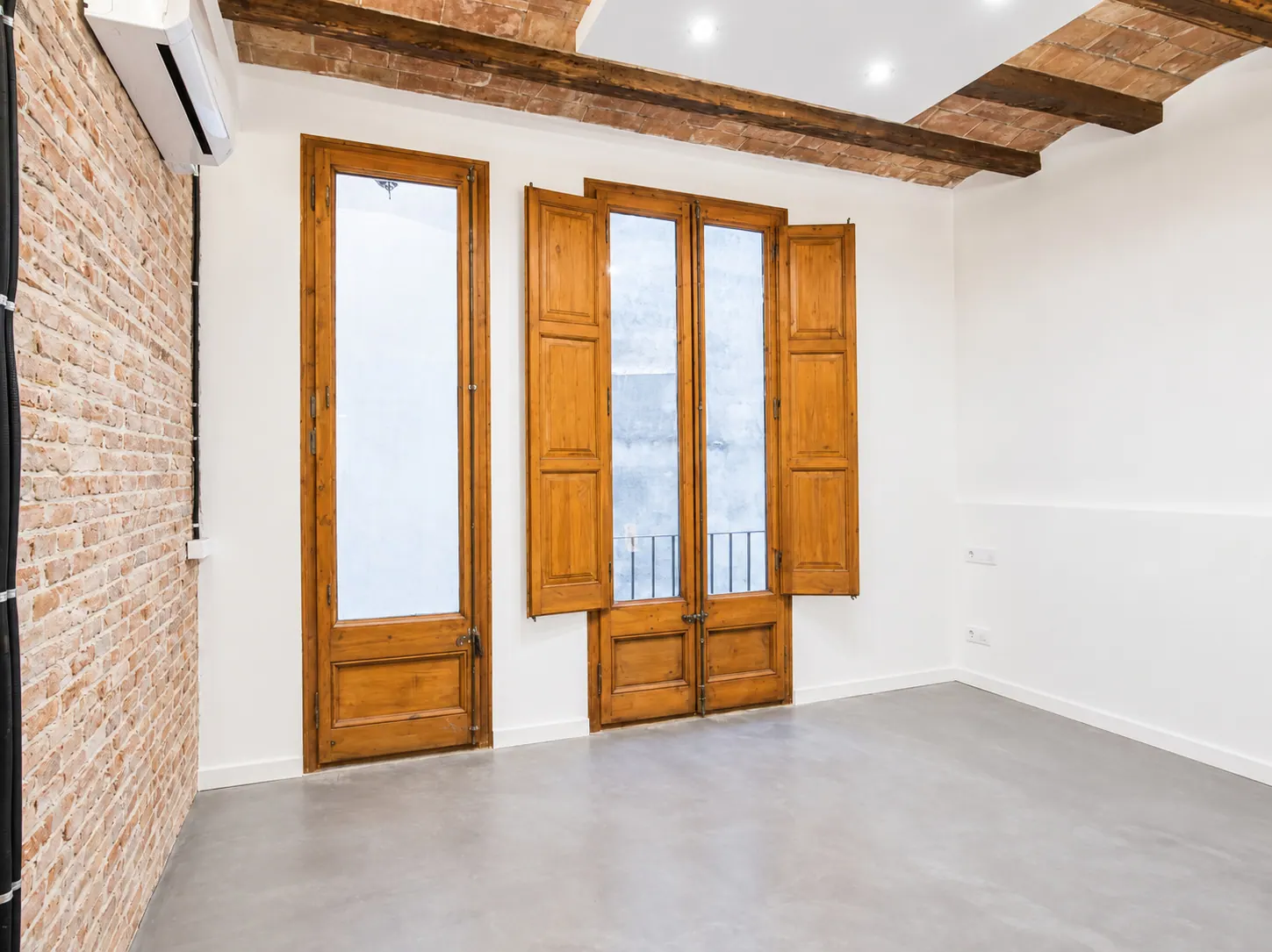 AvN bright room with grey floor, exposed brick and tall balcony doors with integrated shutters