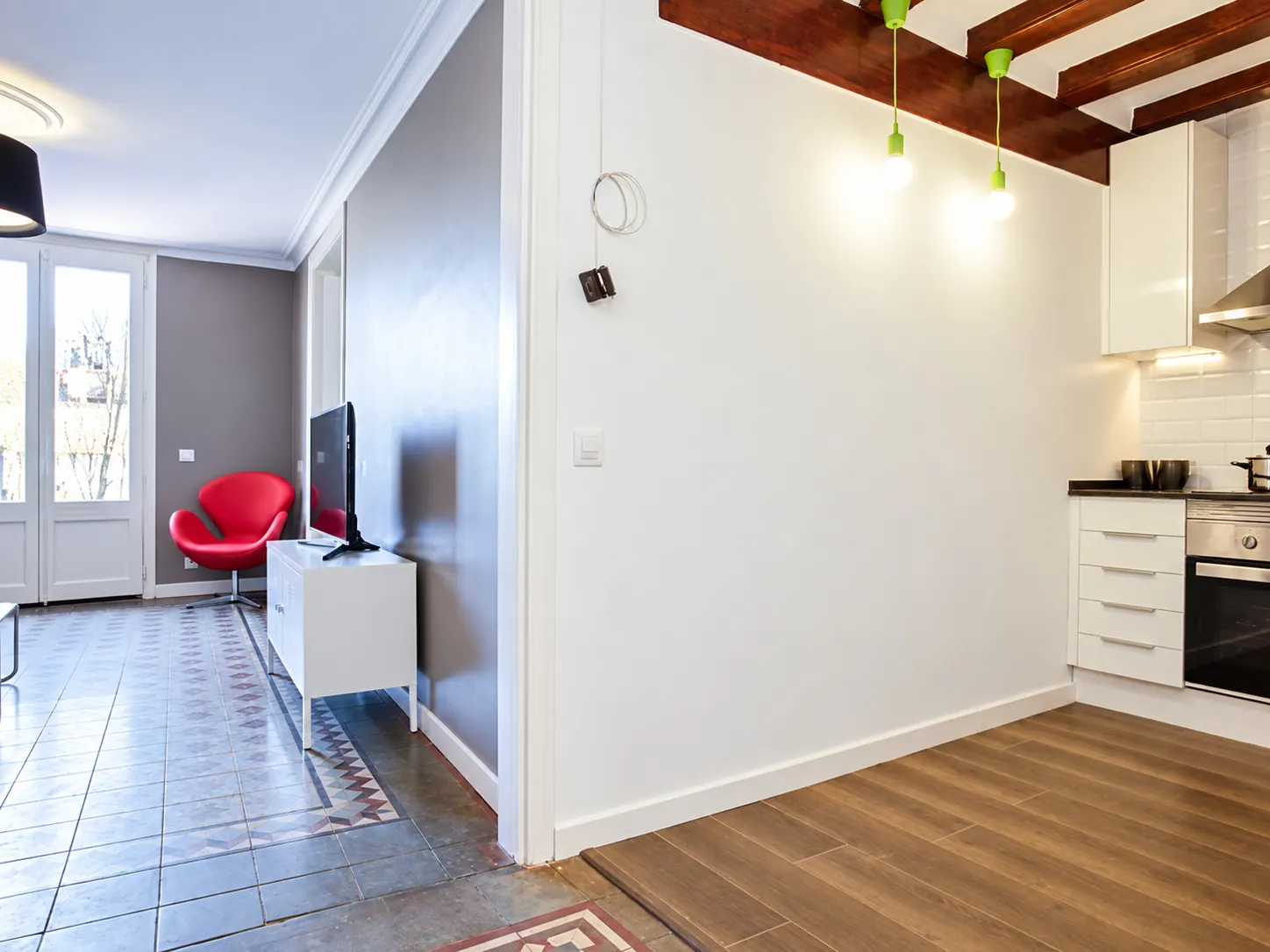 LLn living room with red armchair and television beside the kitchen with green pendant lights