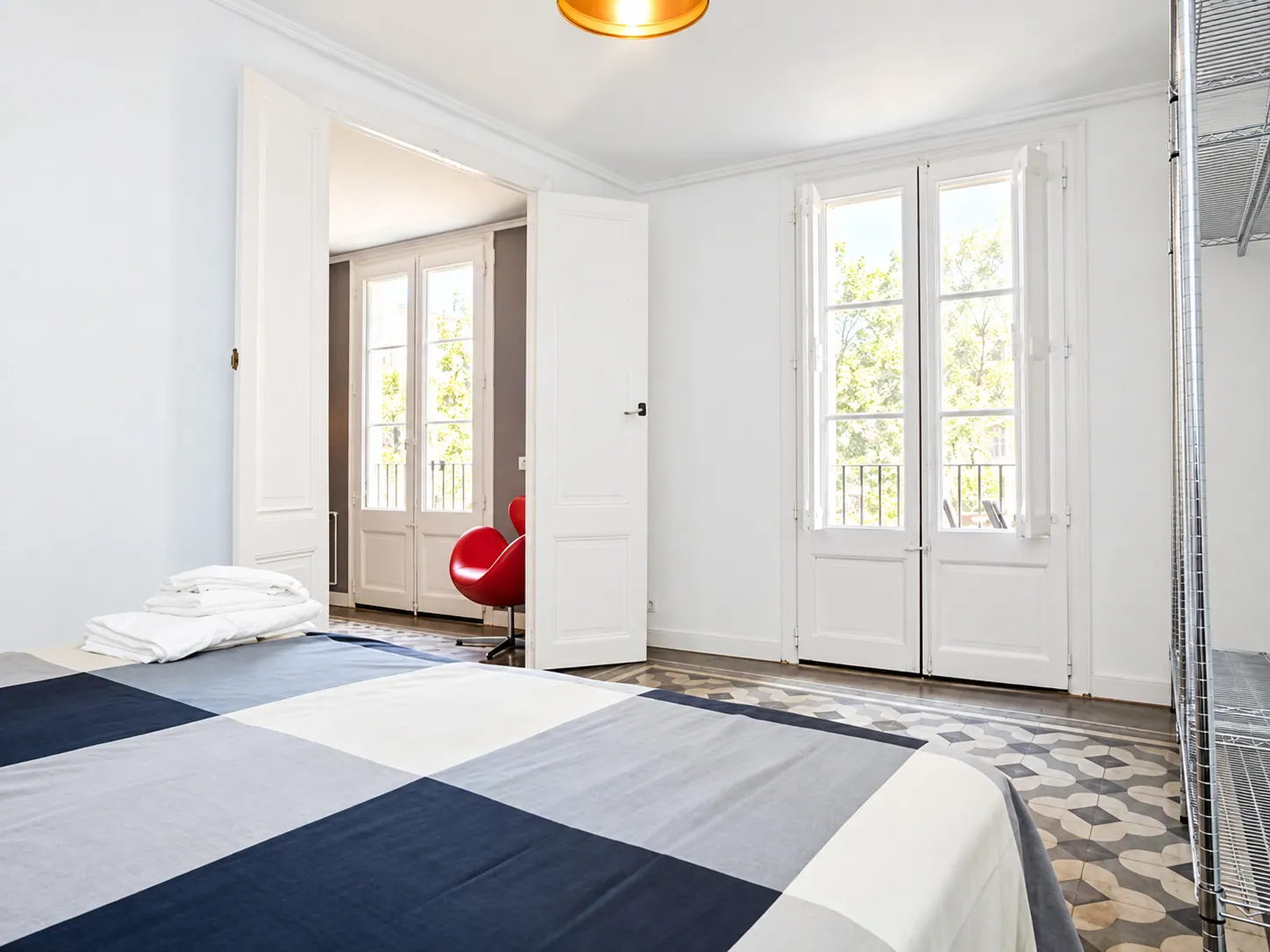 LLn bedroom with white walls, balcony doors with shutters and red armchair in the adjoining room